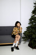 © Irina Ozhigova/Stocksy - Fashionble girl  on a couch near a Christmas tree in a studio