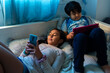 © Jimena Roquero/Stocksy - Hispanic Brother and sister using electronic devices on the bed.