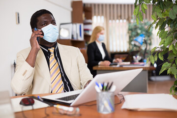 Wall Mural - Businessman in protective mask working alone with laptop and papers in office