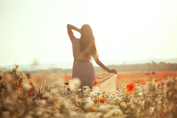 Beautiful girl in summer dress walks in a flower field