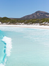 Clear Blue Wave Breaking, White Beach, Dunes Covered In Vegitation And Mountain In The Background
