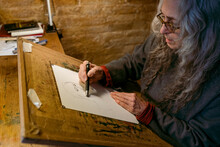 Mature Artist Drawing On A Cork Board Sitting In Her Desk