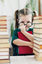 Cute Little Girl In Green Dress With Red Book In Her Hands Fixing A Glasses On Her Nose. Reading And Education Concept