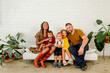 © Erin Brant/Stocksy - Happy biracial family seated on bench in front of white wall