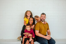 Fun Biracial Family Seated On Ledge In Front Of White Wall