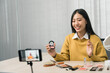 © wutzkoh - Young asian woman vlogging about cosmetics skin care items products on table with her video camera and demonstrates product use and reviews for her online blog channel.