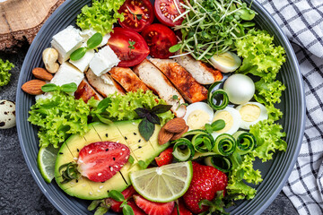 Buddha bowl dish with chicken fillet, quinoa, avocado, avocado, feta cheese, quail eggs, strawberries, nuts and lettuce. Detox and healthy superfoods bowl concept. Food recipe background