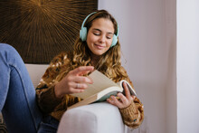 Young Woman In Headphones Reading Book On Sofa