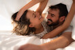 © Atolas/Stocksy - Young couple cuddling and smiling under the bed sheets