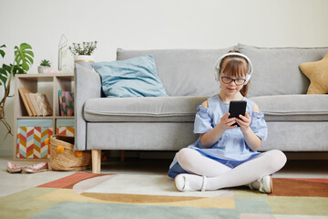 Wall Mural - Candid full length portrait of teenage girl with down syndrome listening to music at home while sitting on floor in cozy interior, copy space