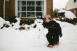 © Maria Manco/Stocksy - boy hugging snowman in front of house