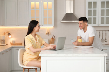 Canvas Print - Happy couple wearing pyjamas with gadgets spending time together in kitchen