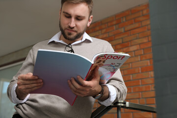 Wall Mural - Young business man reading sports magazine indoors