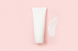 White squeeze bottle plastic tube and big smear of moisturizer on pink background. Natural organic spa cosmetics concept, flatlay, top view. Mockup, template.