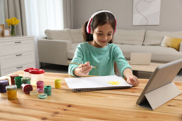 Canvas Print - Little girl with headphones drawing on paper at online lesson indoors. Distance learning