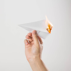 A hand holds a burning paper airplane. Close up. Isolated on a gray background