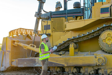 Wall Mural - Hipster construction manager with a beard and safety helmet inspects a work machine. heavy machinery, excavator