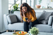 © nenetus - Worried exhausted woman looking her smartphone while waiting for news sitting on couch at home.