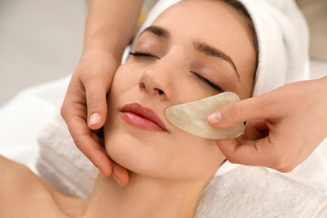 Poster - Young woman receiving facial massage with gua sha tool in beauty salon, closeup