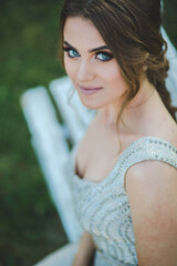 Canvas Print - Attractive Caucasian female wearing an elegant long silver dress sitting on a bench in a park