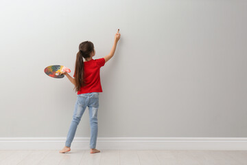 Poster - Little girl painting on light grey wall indoors, back view. Space for text