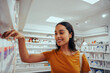 © StratfordProductions - Portrait of smiling young woman in drugstore standing against shelf picking medicine
