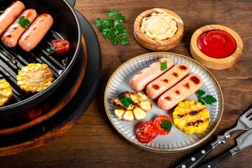  Grilled sausages with vegetables and sauces. Summer BBQ with sausages, corn and tomatoes on the wooden table