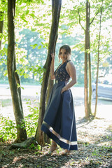 Poster - Attractive Caucasian female wearing an elegant blue dress leaning on the tree in a park