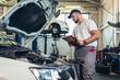 © Mediteraneo - Man writing on a clipboard in a garage.