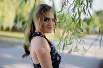 Poster - Attractive Caucasian female wearing an elegant dark blue dress seen through tree leaves in a park