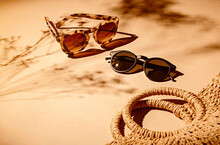2 Pairs Of Women Sunglasses And A Bag On A Soft Orange Background And Strong Shadows Of Flowers