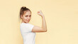 Strong powerful confident caucasian young blonde woman raises arm and shows bicep isolated on a light color beige background. Feminism, girl power, equal women's rights and independence concept