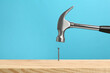 © New Africa - Hammering nail into wooden surface against light blue background
