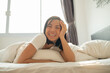 © nareekarn - Portrait of beautiful young asian woman with attractive smile enjoy fresh bedding linen mattress in white bed room apartment.woman sleep resting, good night. Portrait of happy young woman lying in bed