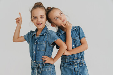 Blonde two girls dressed overalls pointing finger and looking upward