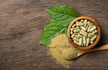 Wall Mural - Flat lay of Kratom (Mitragyna speciosa) capsules with powder and fresh leaf on wood background.