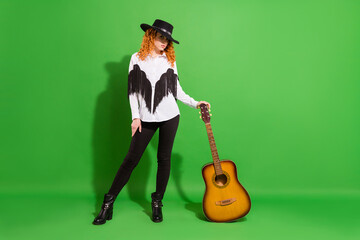 Full length body size view of attractive serious girl posing holding guitar isolated over bright green color background