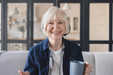 Wall Mural - Video call front view image businesswoman using a laptop for remote work from home office. Elderly IT support worker in headset having a video conference, online meeting. Senior teacher leads webinar