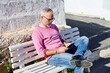 © Ivan Gener/Stocksy - Mature man using a tablet on a bench