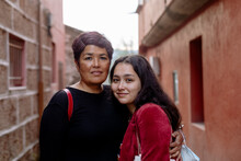 Close Up Mother And Young Adult Daughter Hugging By Red Walls In Road