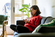 © Malquerida Studio/Stocksy - Young woman browsing smartphone sitting in a sofa at home