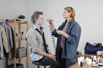 Wall Mural - Mature female makeup artist applying grey greesepaint on businessman face with special equipment