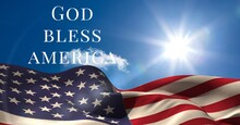 Composition Of Text God Bless America Over Waving American Flag On Sunny Blue Sky