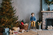 © Alina Hvostikova/Stocksy - Cute boy sitting on stool near Christmas tree and presents