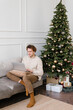 © Alina Hvostikova/Stocksy - Serious young guy using laptop sitting on sofa near decorated Christmas tree at home