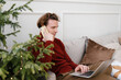 © Alina Hvostikova/Stocksy - Concentrated young man talking on smartphone and using netbook on sofa during Xmas holidays