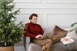 © Alina Hvostikova/Stocksy - Concentrated young man talking on smartphone and using netbook on sofa during Xmas holidays