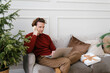 © Alina Hvostikova/Stocksy - Concentrated young man talking on smartphone and using netbook on sofa during Xmas holidays