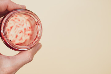 Poster - Closeup of a hand holding an open empty strawberry jam jar isolated on light brown background