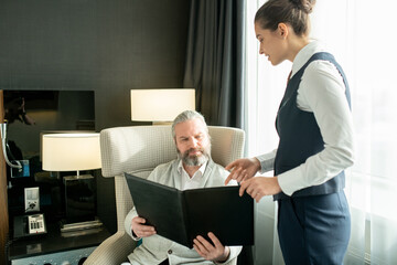 Wall Mural - Young female manager recommending something from menu to mature man